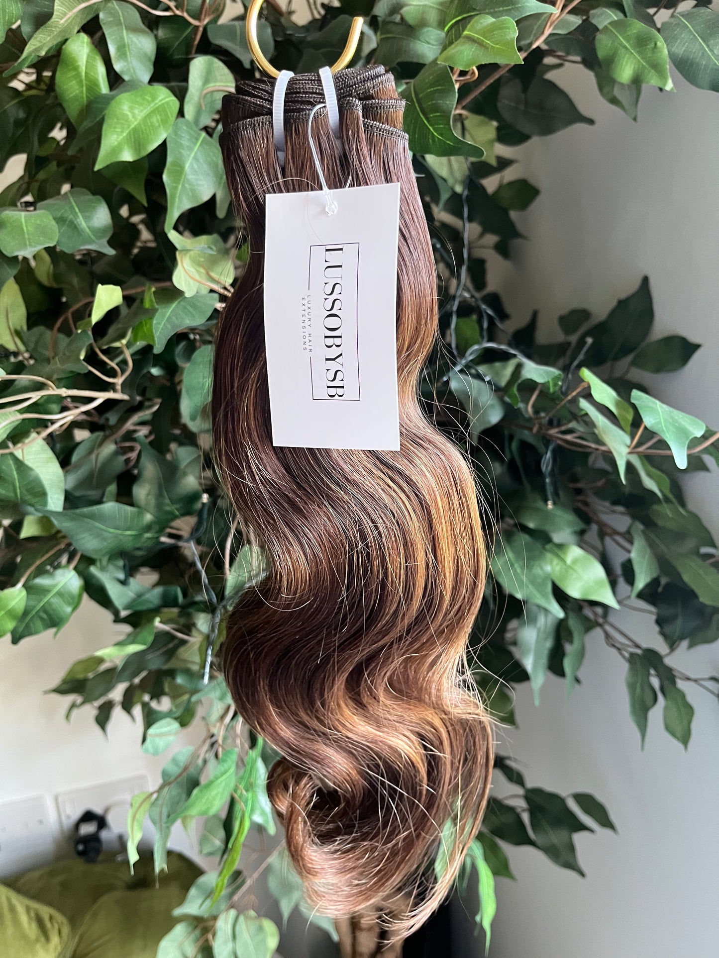 Ava's Glow wavy hair extensions by LUSSOBYSB, nestled among green foliage. These luxurious, pre-highlighted Golden Blond hair bundles offer a stylish way to enhance your look with effortless wave and shine.