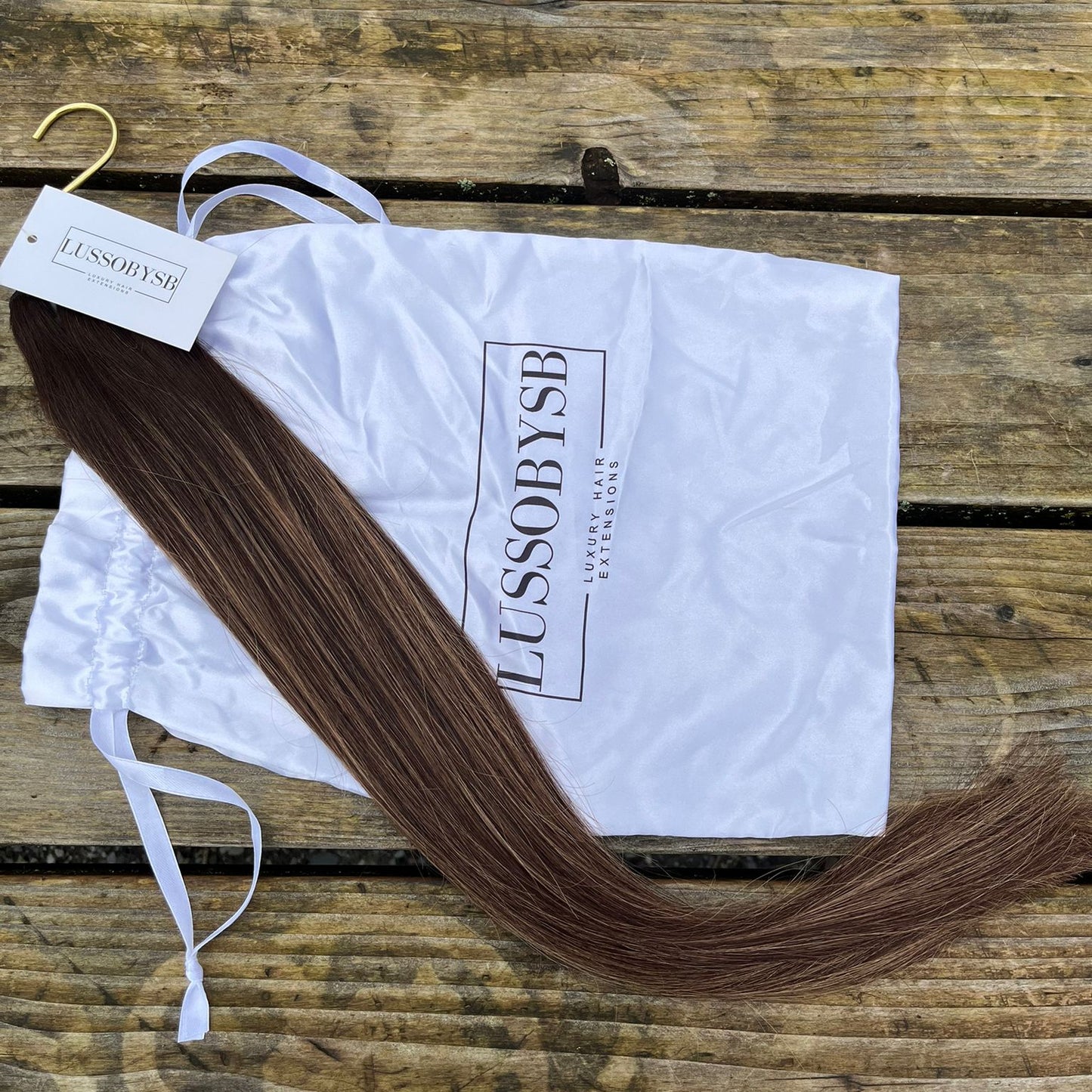 Ava's Glow hair extensions by LUSSOBYSB displayed on a wooden surface, featuring silky, straight strands. Ideal choice for adding volume and length, these hair extensions are part of the Golden Blond Pre-highlighted hair bundles collection.